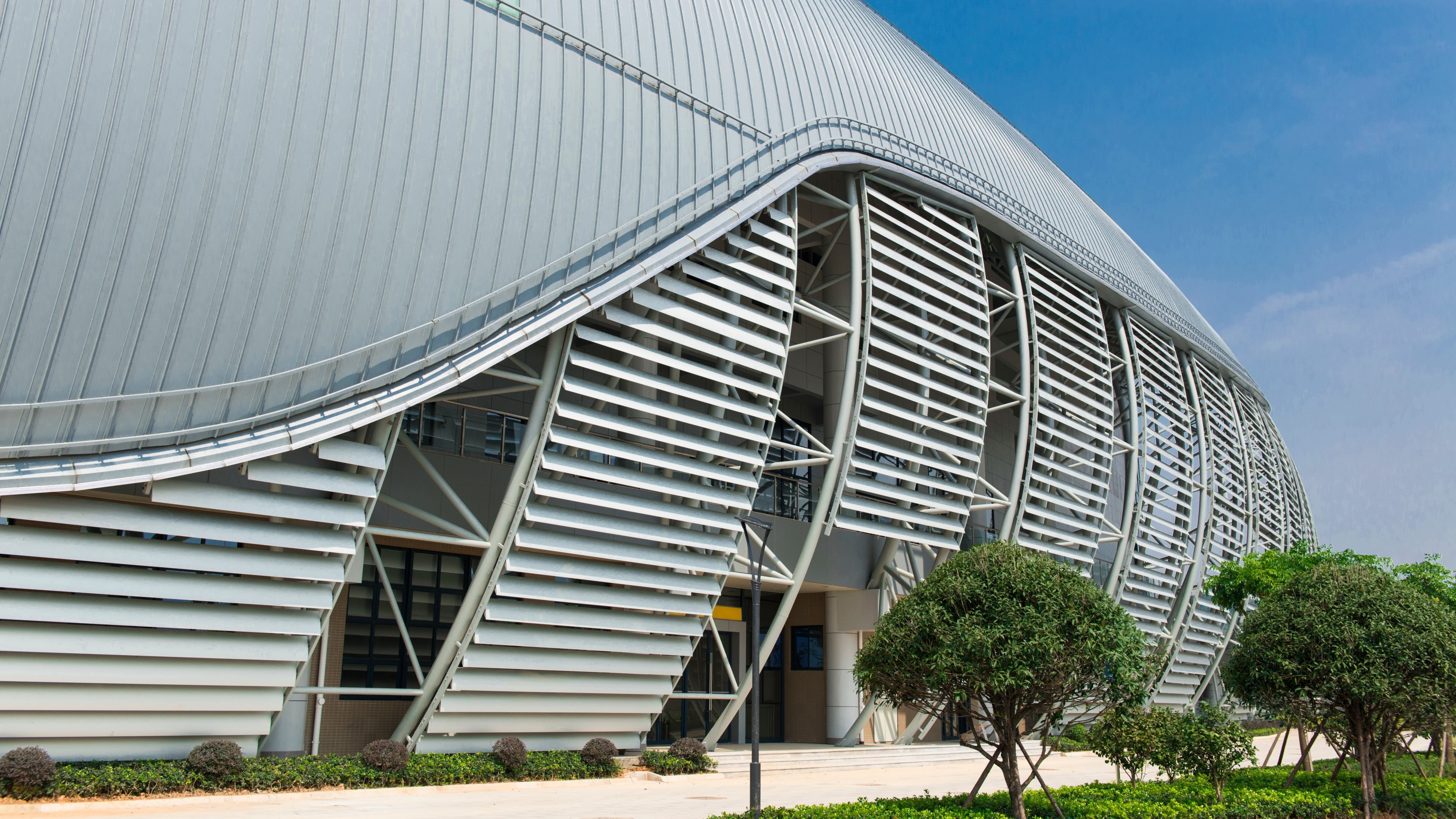 Curved sports center facade with horizontal sun louvers in Lianjiang