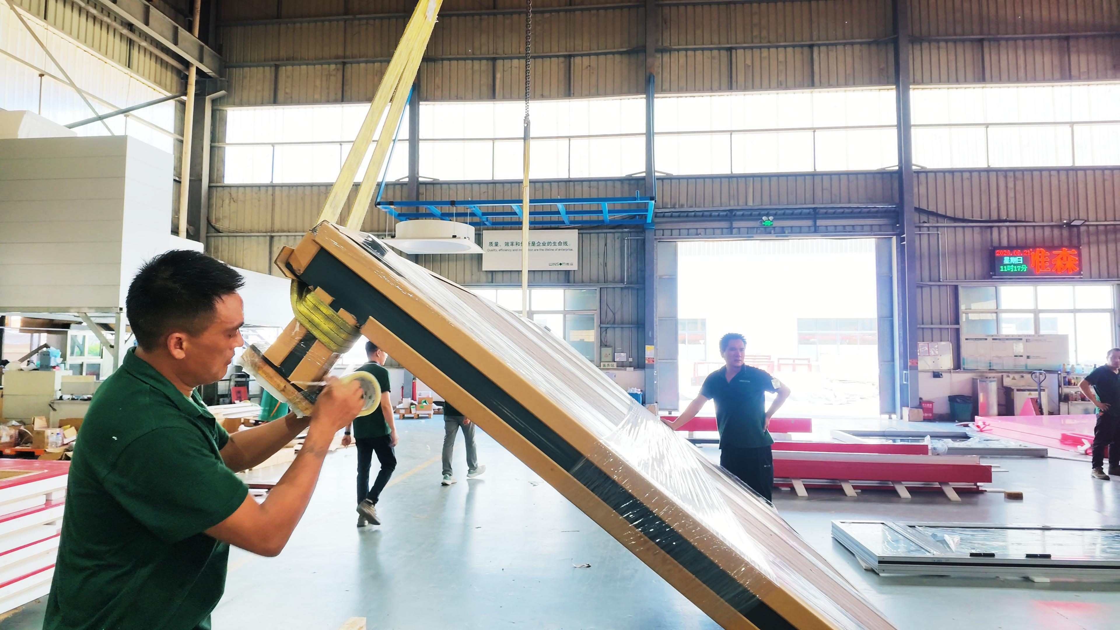 Workers applying protective packaging to a building component at the factory