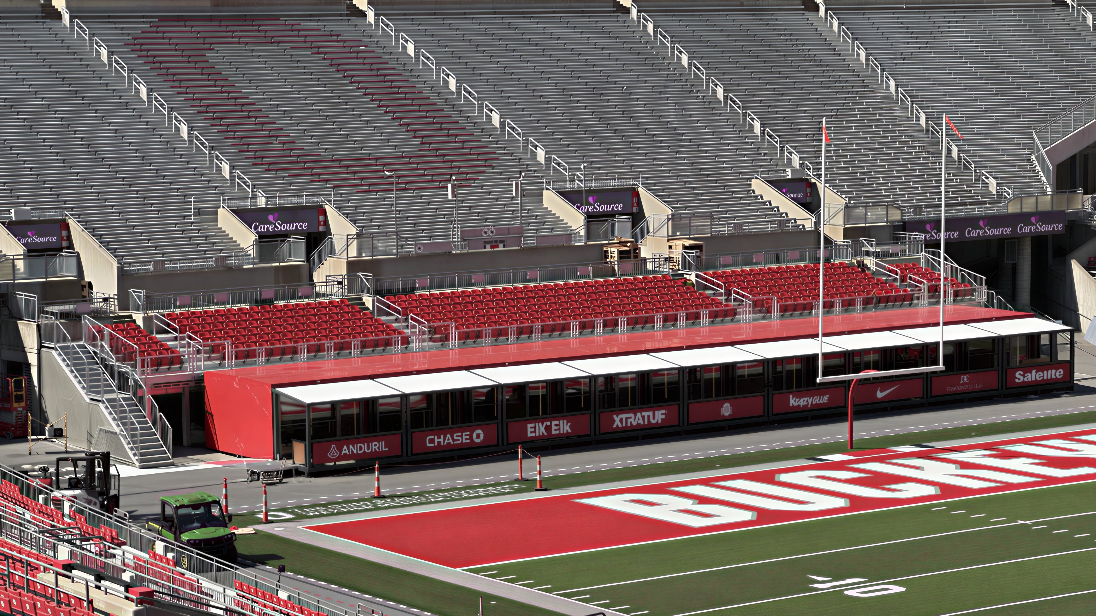 Red stadium hospitality suites with covered viewing terraces beside the football field and tiered seating